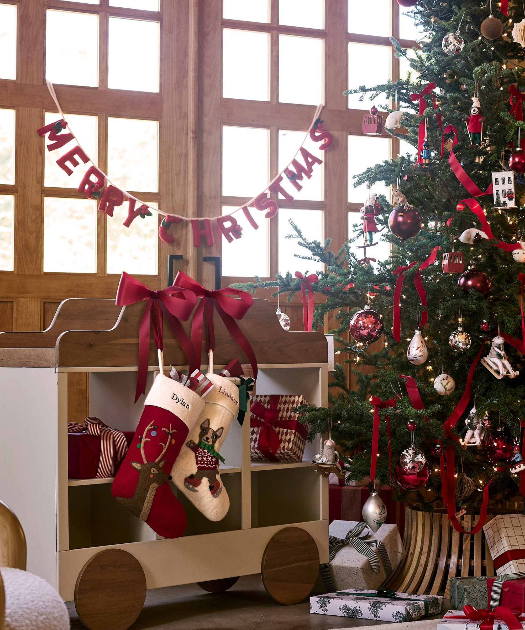 a Christmas display with a tree decorated with ornaments, two stockings, a felt banner that says &#039;Merry Christmas&#039; and two bows