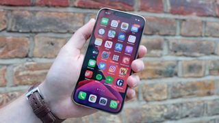 Ein iPhone 13 Pro in der Hand eines Mannes, mit einer Ziegelmauer dahinter