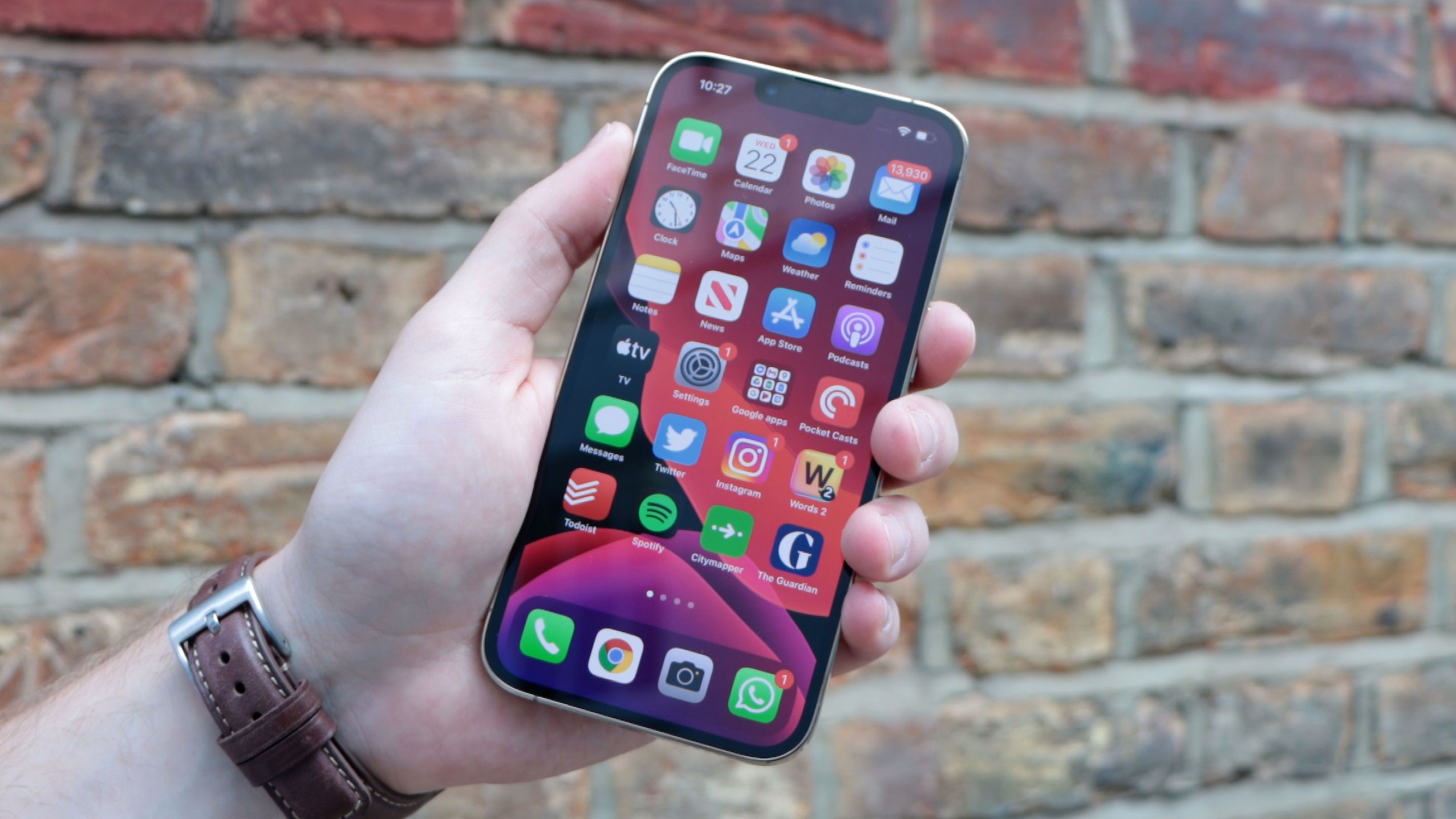 An iPhone 13 Pro held in someone's hand with a brick wall in the background