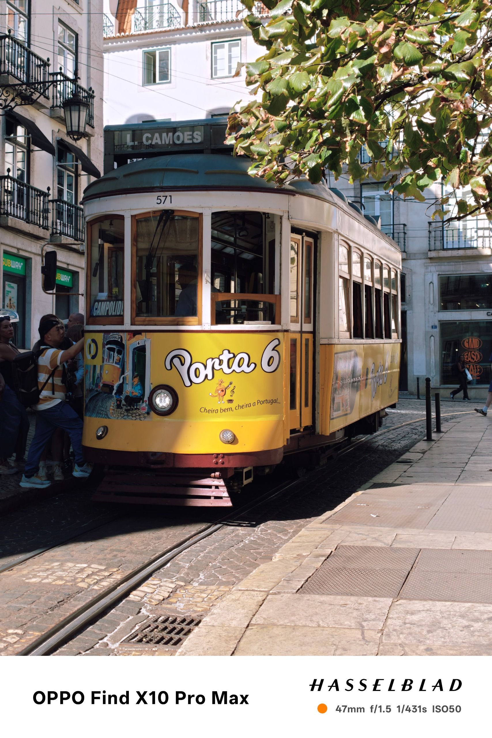 Yellow Lisbon tram traveling along tracks through a sunlit city street.