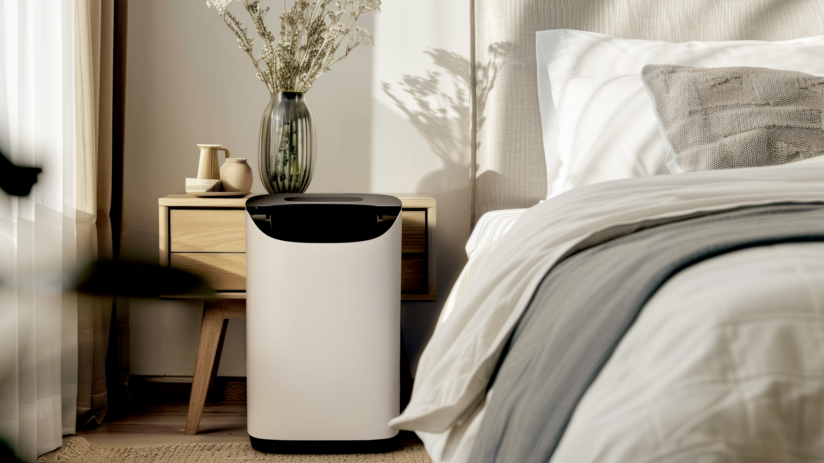 Meaco DD8L Pro Desiccant dehumidifier in a bedroom with neutral bedding, sheer curtains and oak bedside table