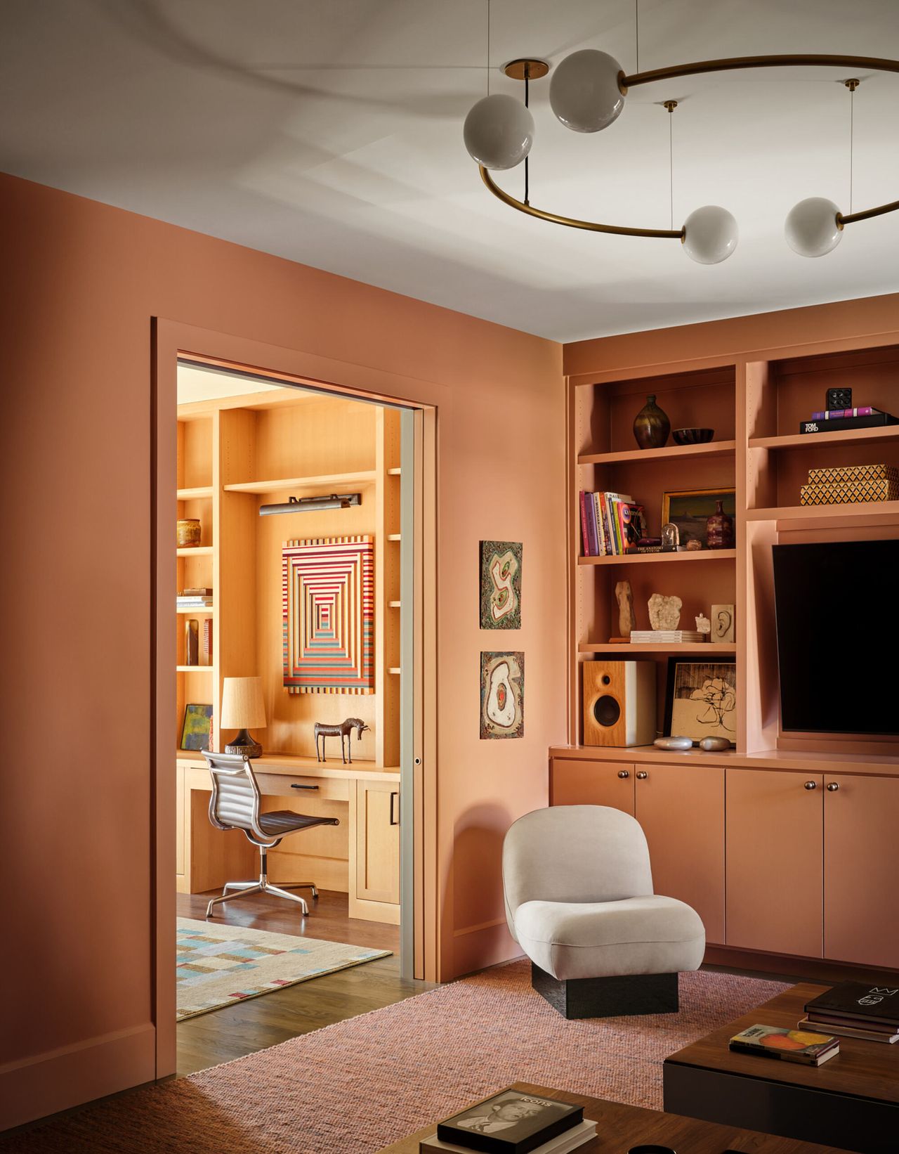 media room with built-in bookshelves around TV, armchair, peach-colored walls, and statement pendant light