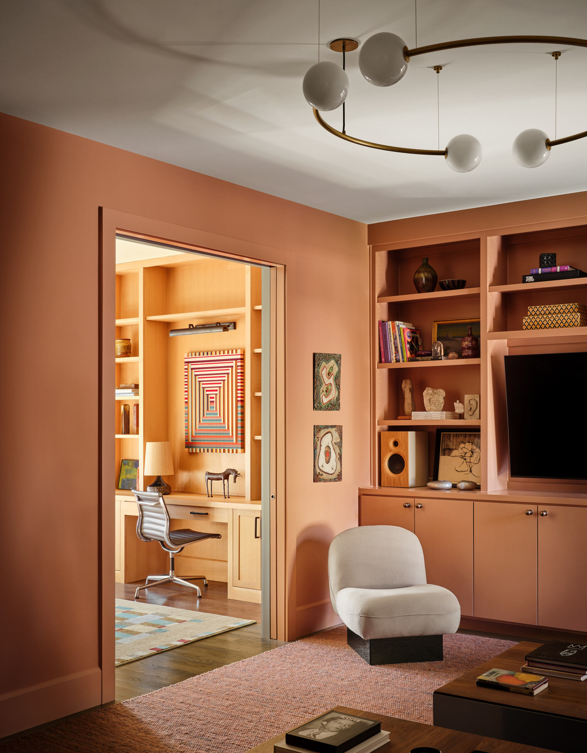 media room with built-in bookshelves around TV, armchair, peach-colored walls, and statement pendant light