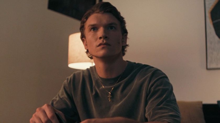 Connor Storrie as Ilya looking in shock at the TV. 