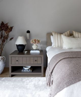 gray farmhouse style bedroom with a large nightstand styled with a small black lamp and a wall sconce