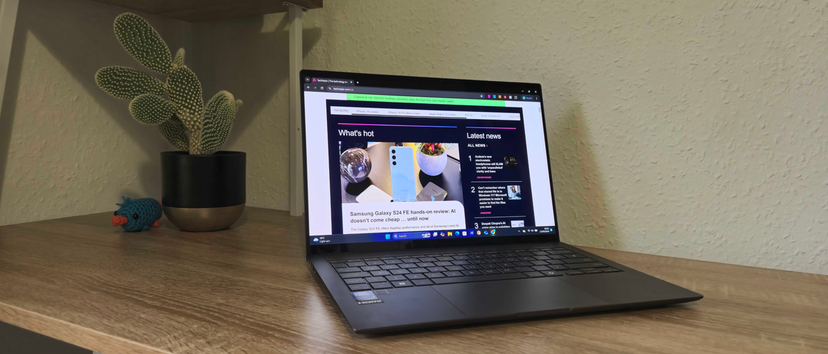 The Asus Zenbook S 14 on a desk in front of a cactus, the screen shows the TechRadar home page