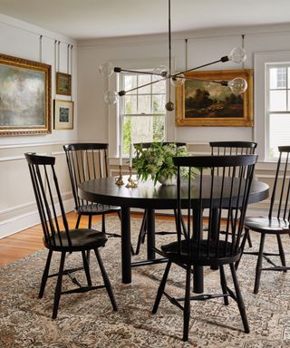 Dining room with round black dining table, matching chairs, rug, artwork on walls, sculptural black metal pendant light over table