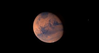 A rusted red planet hangs in black space, its face scarred with black canyons and dark dusty seas.