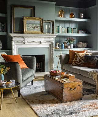 pastel living room ideas, green living room with grey couches, wooden trunk, vintage frames, shelving in alcoves, ornaments, orange cushions