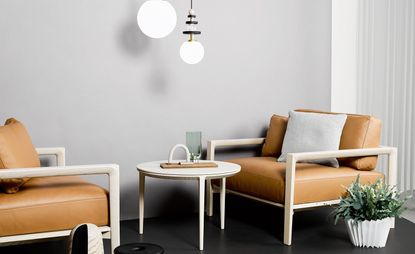 A beige, round coffee table is set between two leather armchairs in orange-brown color, with matching beige arms and legs.