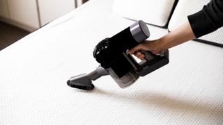 Image shows a person vacuuming a white mattress before cleaning mold off of it