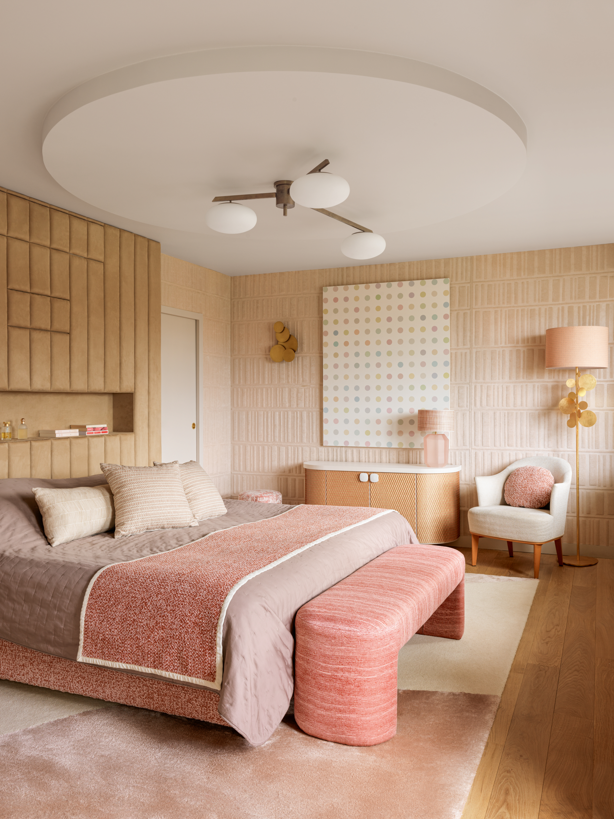 Bedroom with beige textured walls, built-in headboard, pink bed and bench, pink and white rug and oak console