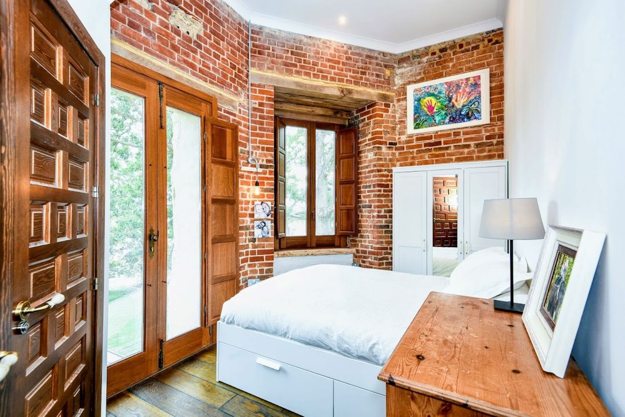 The bed has a white covering and sits opposite the bifold windows leading out to the balcony and is surrounded by brown brickwork