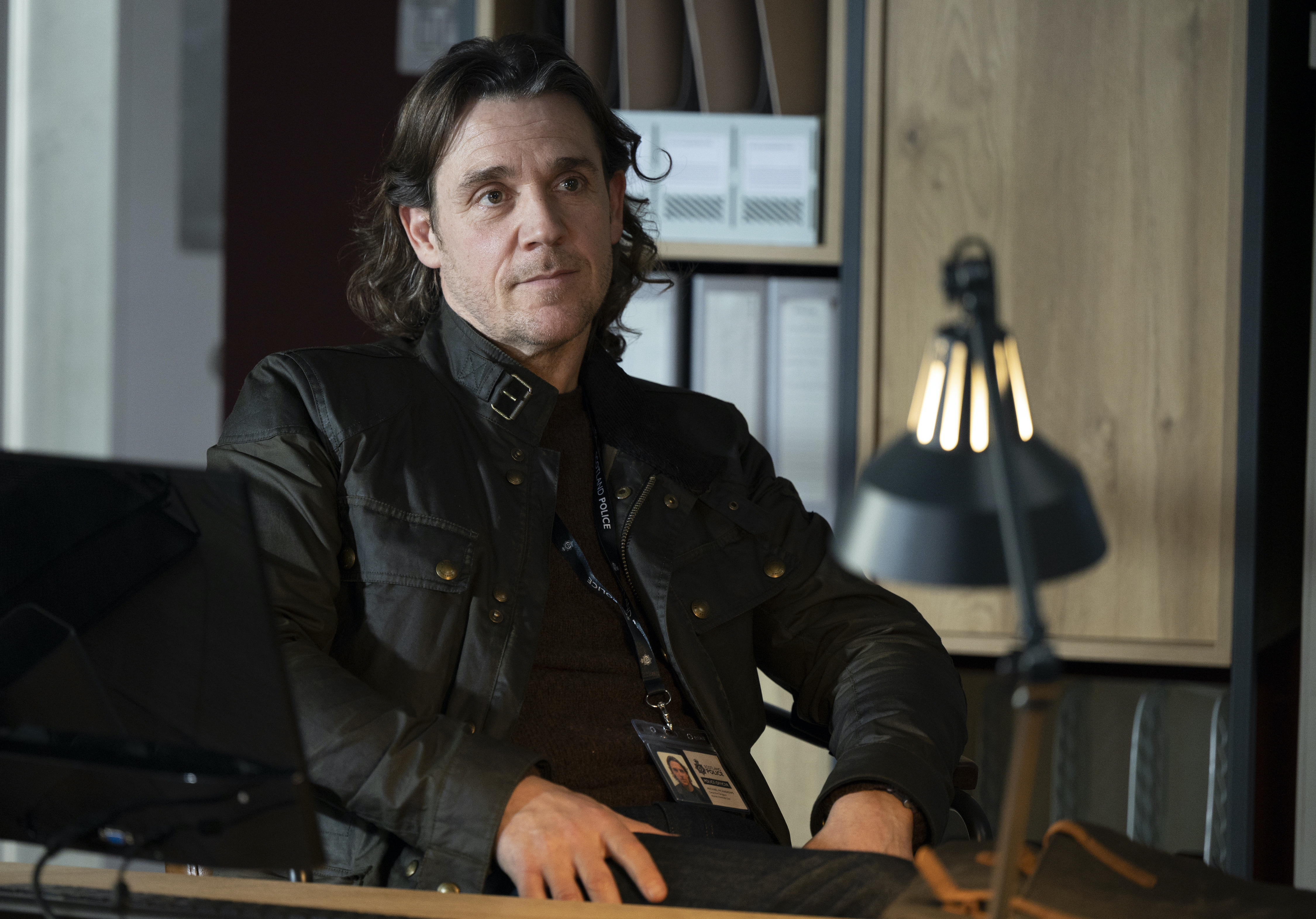 DS Michael McAndrews (Jamie Sives), dressed all in black, sits in a chair in the Marine Homicide Unit's office