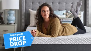 A woman lying on a Sealy Cool 12" Medium Memory Foam Mattress, with a Tom's Guide badge overlaid saying "PRICE DROP"