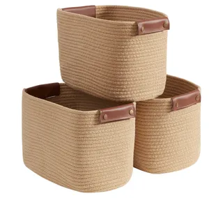 Three brown woven storage baskets with dark brown leather handles. Two on the bottom with a third stacked on top. on a white background.