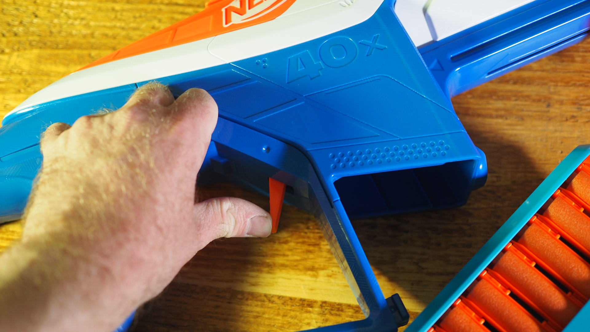 A Nerf N-Series Infinite blaster lying on a wooden table while a hand presses the ammo release lever