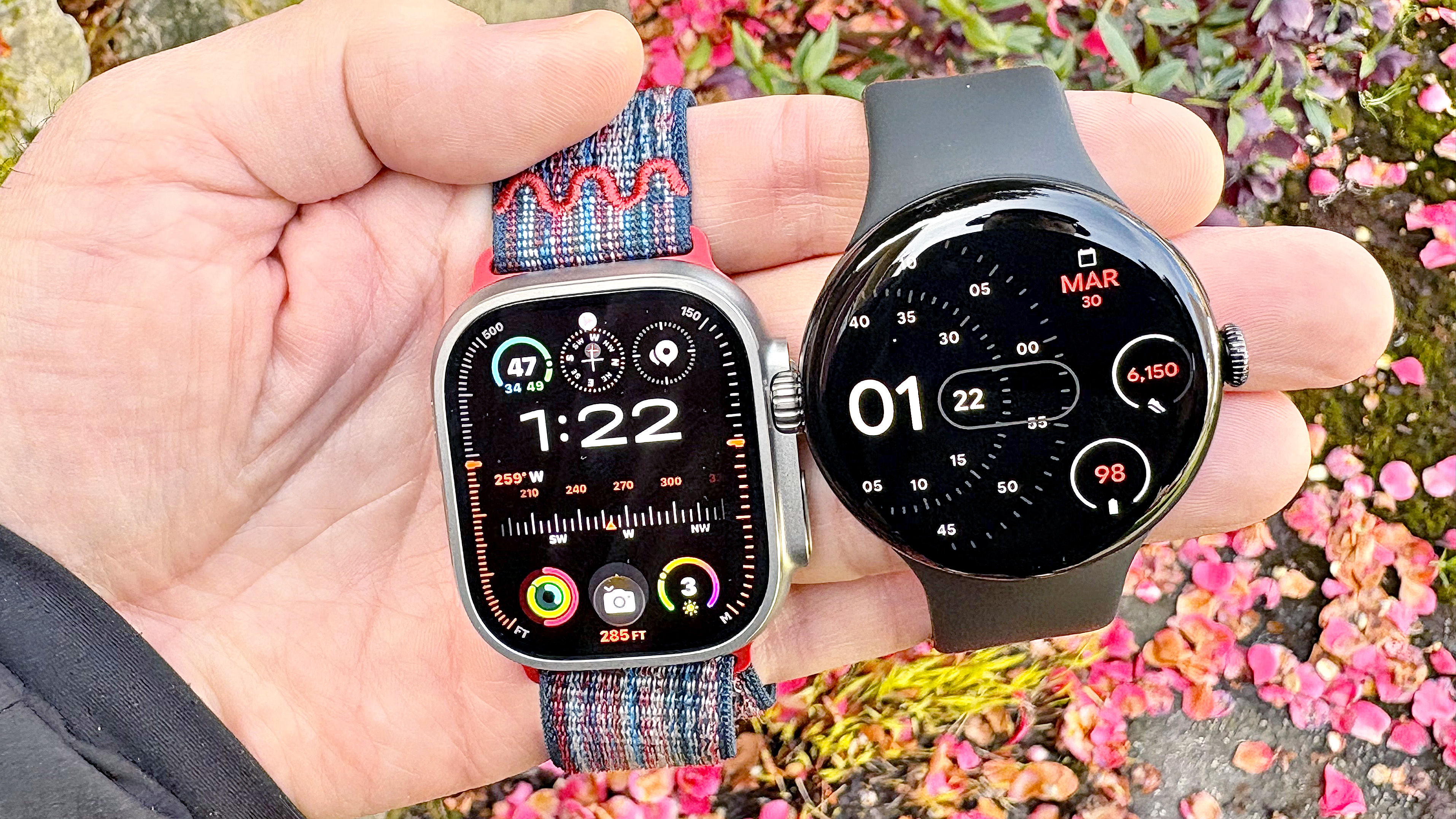 Close-up of the Apple Watch Ultra 3 and Google Pixel Watch 4 in a user's hand against a colorful out-of-focus background