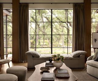 Neutral living room with day bed, large coffee table and large windows looking out onto oak trees