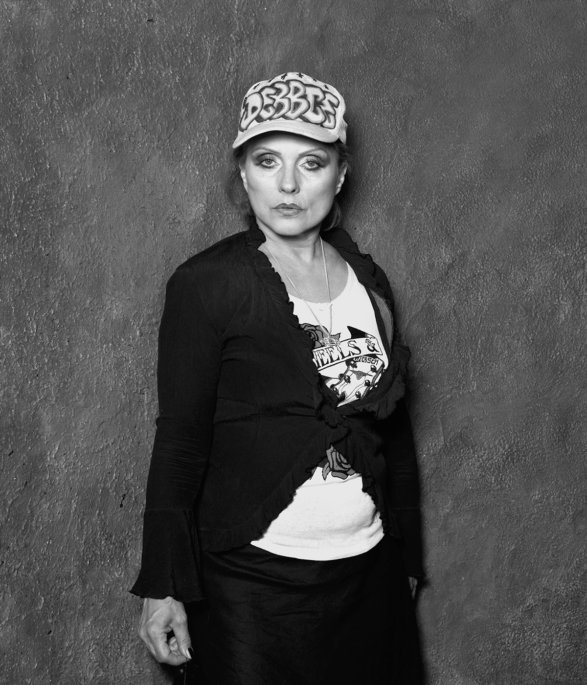black and white portrait of singer Debbie Harry, posing against wall