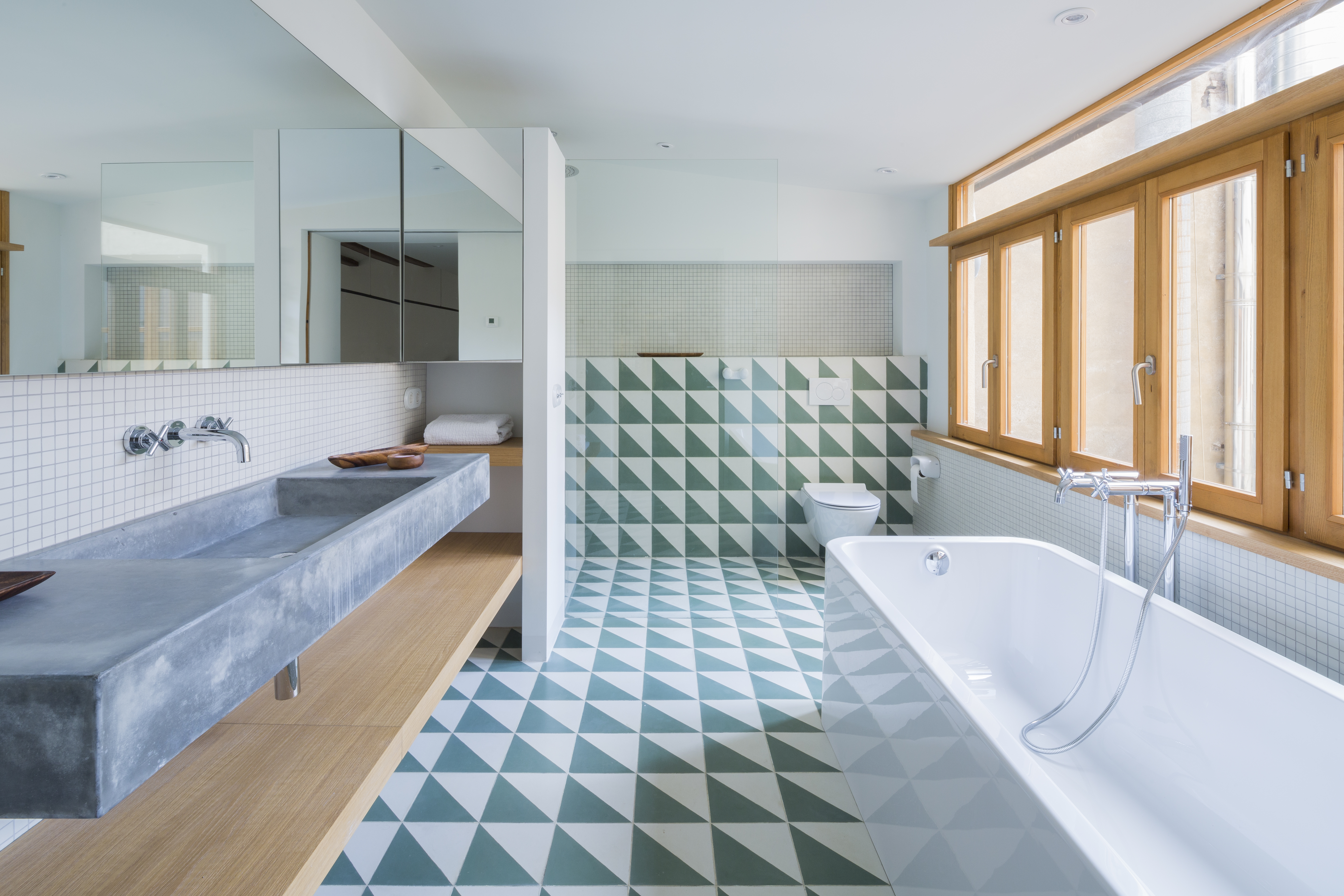 A bathroom with patterned tiles, a large rectangular mirror
