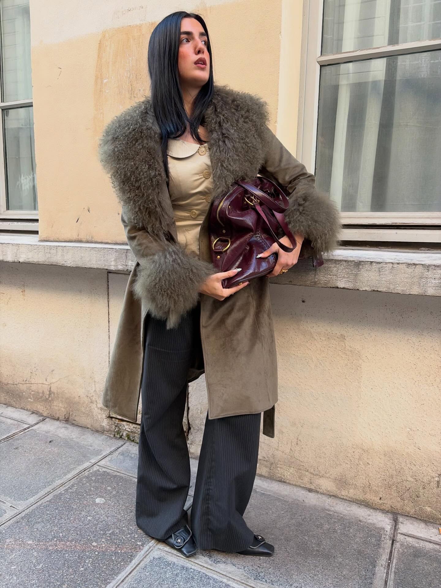 An image of an influencer in Paris in an olive khaki fur-lined coat with wide-leg trousers and holding a slouchy burgundy leather tote