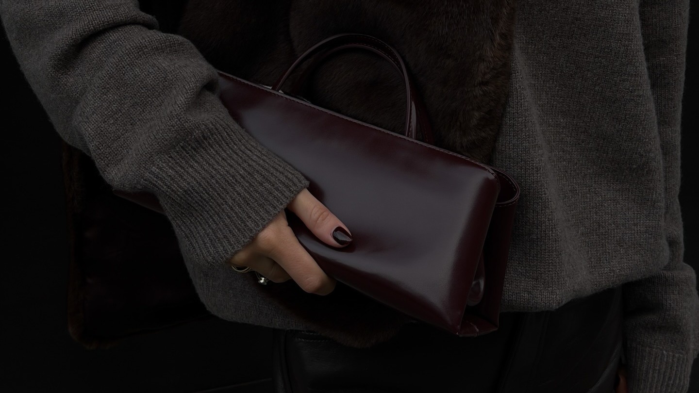 Woman wears a grey sweater, fur stole with silver pin and Verafied's eclair bag in burgundy.