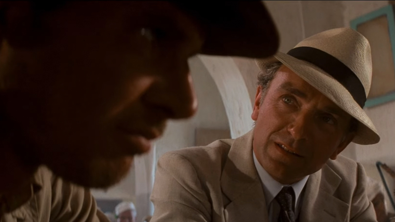 Paul Freeman in a white hat talking to Harrison Ford in the foreground