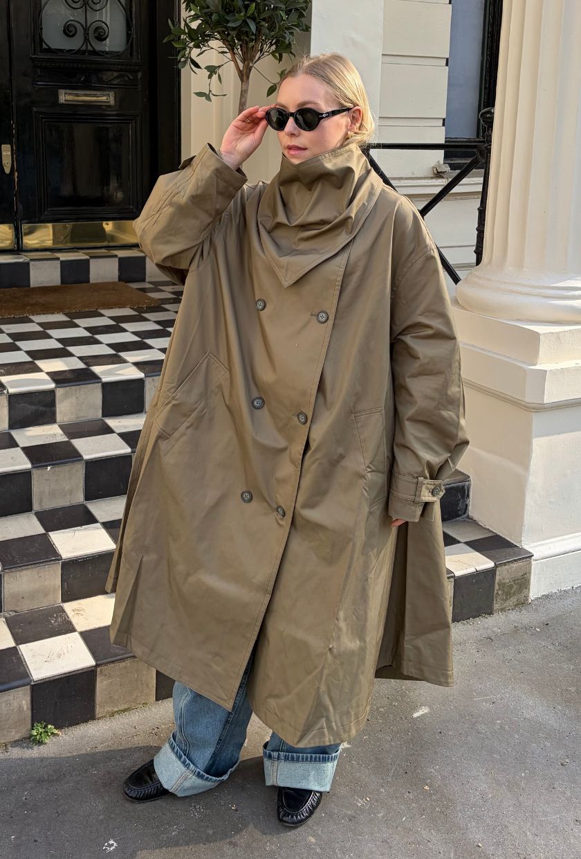 Woman wears beige trench coat, blue jeans and black loafers