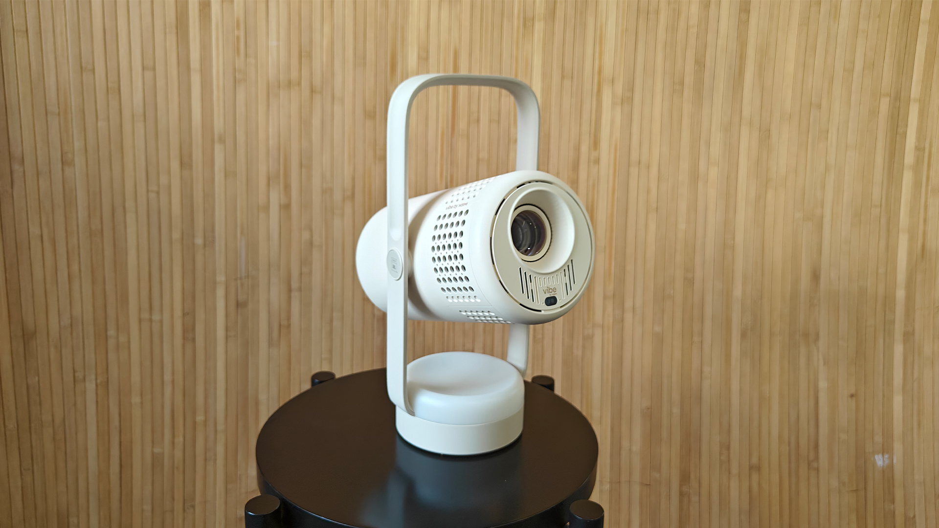 Xgimi Vibe One portable projector on small black table against bamboo effect wall