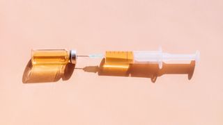 A syringe on a pink backdrop, drawing liquid from a vial