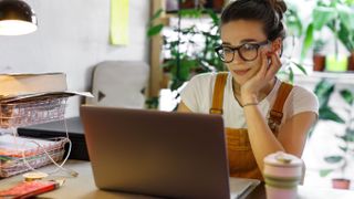 A woman sitting at a desk and using a MacBook, and there's a background of several indoor plants