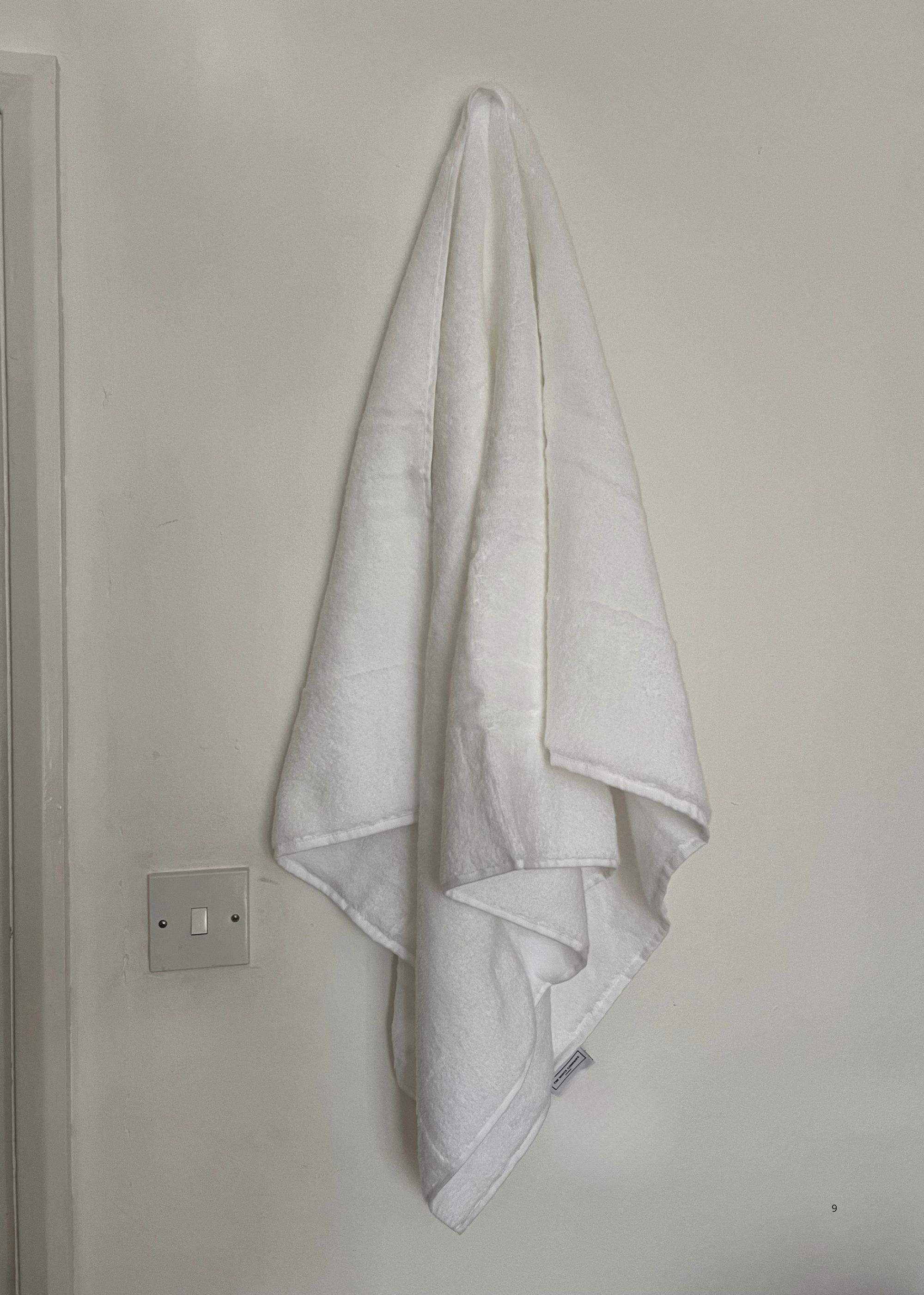 A white towel hanging on a hook against a white wall.