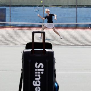 Tennis court with Slinger Bag in foreground and person about to play a shot in background