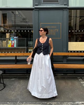 Woman on street wears black waistcoat and white a-line skirt