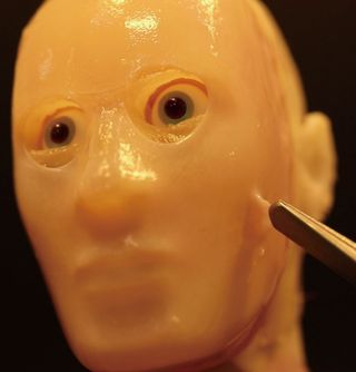 Artificial skin being pulled on sculpted human-like face