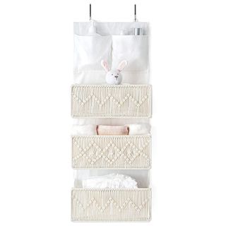 A white bathroom organizer holds a bunny rabbit toy and some towels, and features macrame detailing