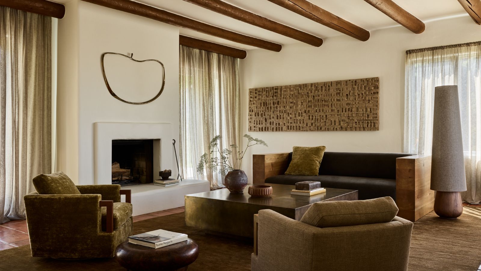 A living room of an Adobe home featuring white plaster walls, exposed wooden ceiling beams and earth tone furniture
