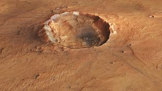 A photo of the surface of Mars from space, with a large crater seen in its reddish brownish surface