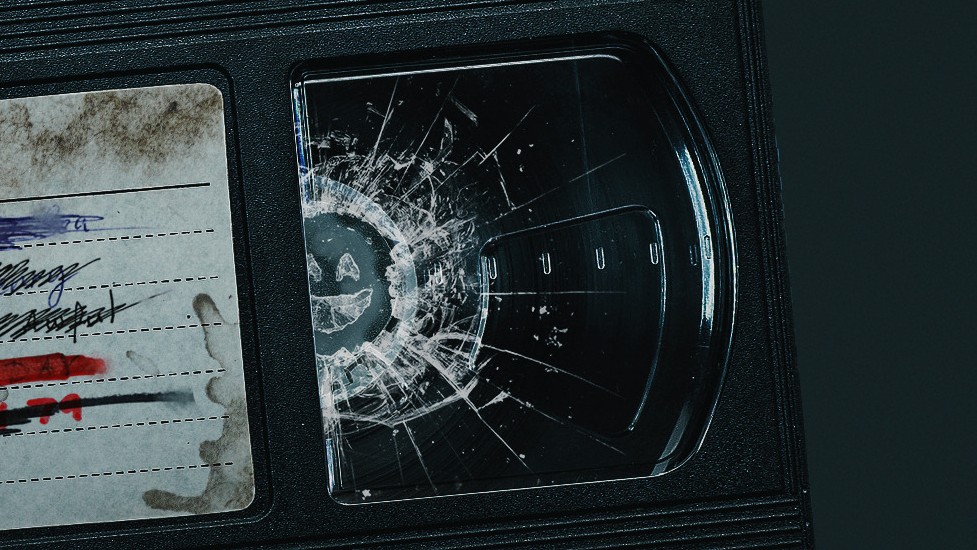 A dirty and used video cassette with a smiley face smashed into the right-hand side (the Black Mirror TV series logo).