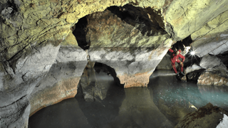 A water-filled cave in Albania with a researcher posing by some rock columns.