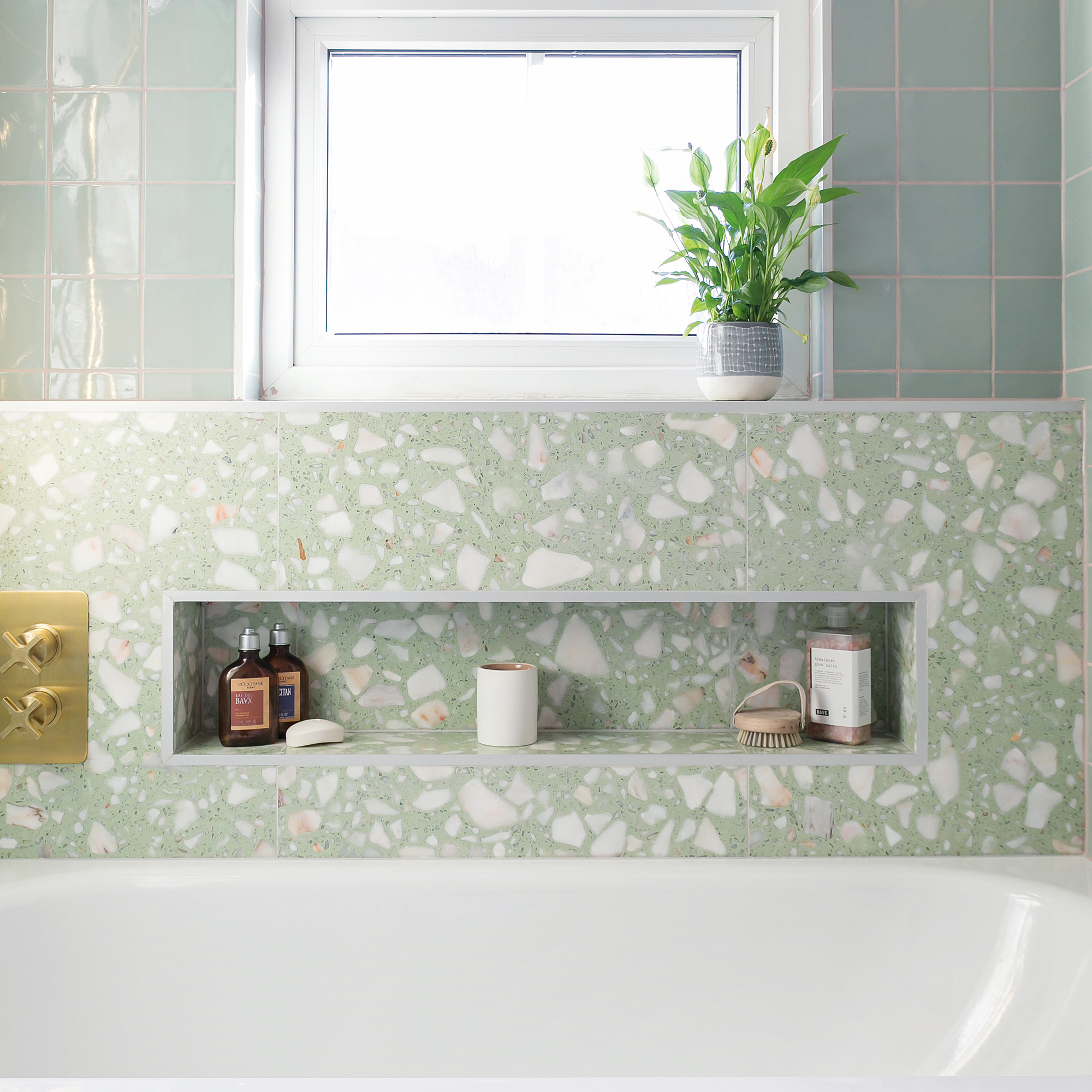 a bath tub beside a window with green terrazzo and green tiles on the wall