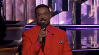 Alfonso Ribeiro wearing an all-red suit holding a mic on DWTS Mariah Night.