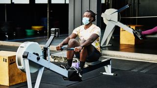 Man wearing protective face mask working out on rowing machine at outdoor gym. Thomas Barwick via Getty Images.