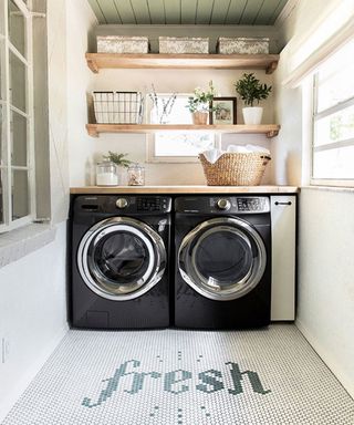 A mudroom laundry area with two black washing machines and a mosaic tiled floor