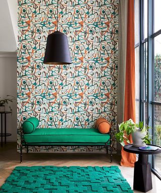 Bohemian living room idea with abstract wallpaper, a chaise in green and orange, green rug and lamp.