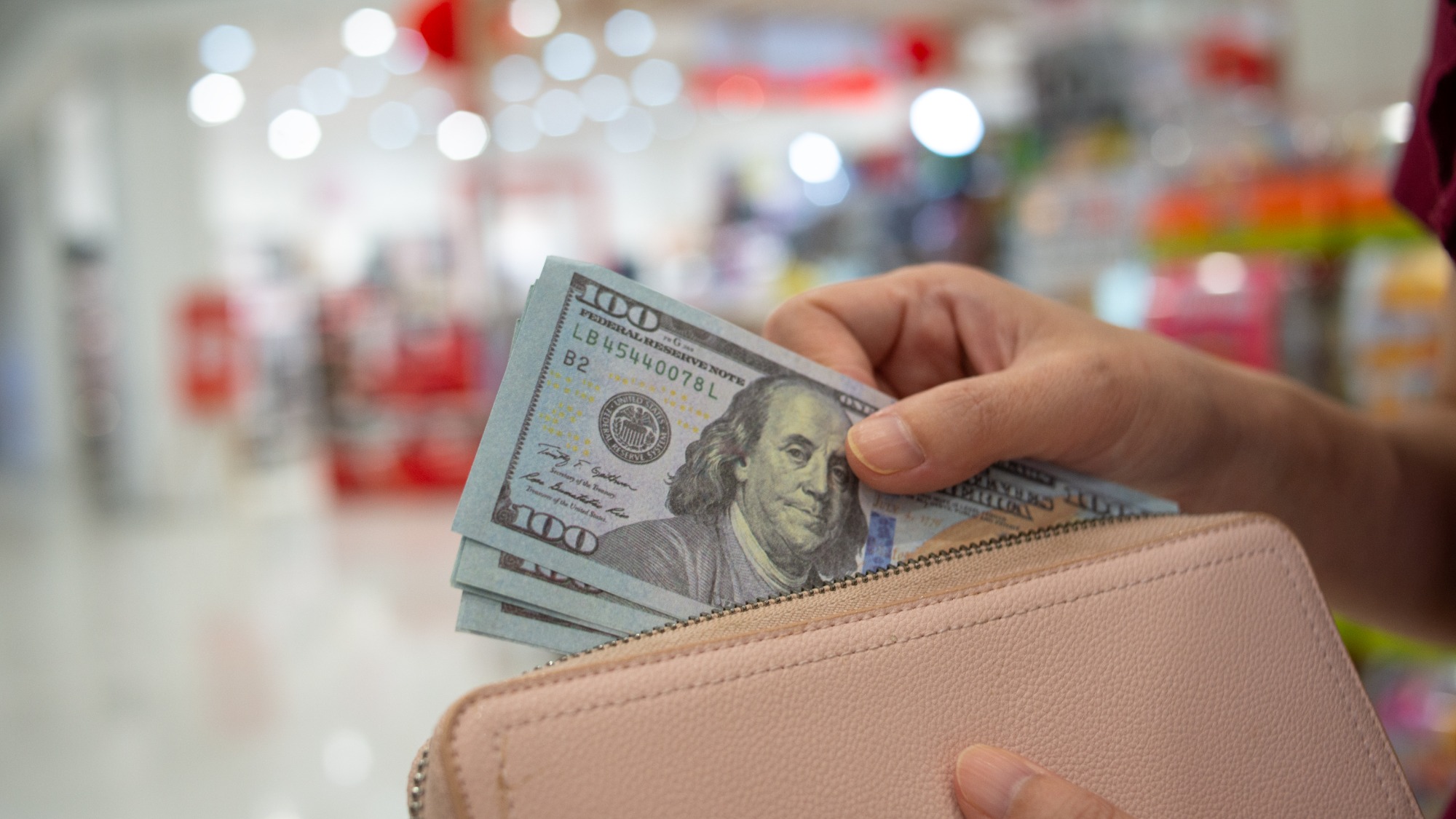 Woman taking stack of 100 dollar bills out of a wallet in a store