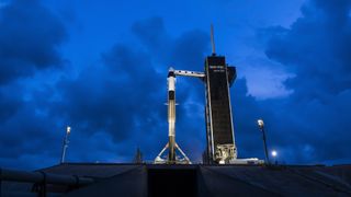 A SpaceX Falcon 9 rocket carrying the Polaris Dawn Dragon capsule stands atop its Florida launch pad for launch with think clouds behind.