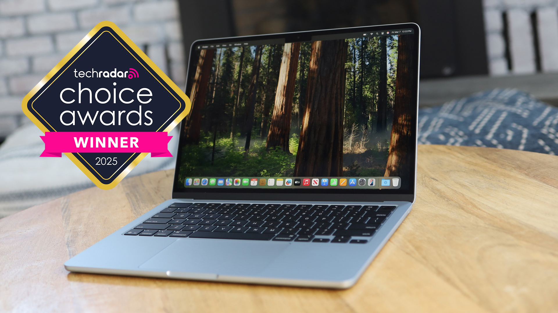 The MacBook Air M5, showing the macOS home screen, on a wooden table, with a logo saying TechRadar Choice Awards 2025 winner