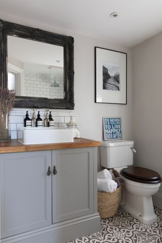 Pippa Jones house: bathroom with grey sink unit, bronze mirror, monochrome pattern floor and 'It's never too late to live happily ever after' print